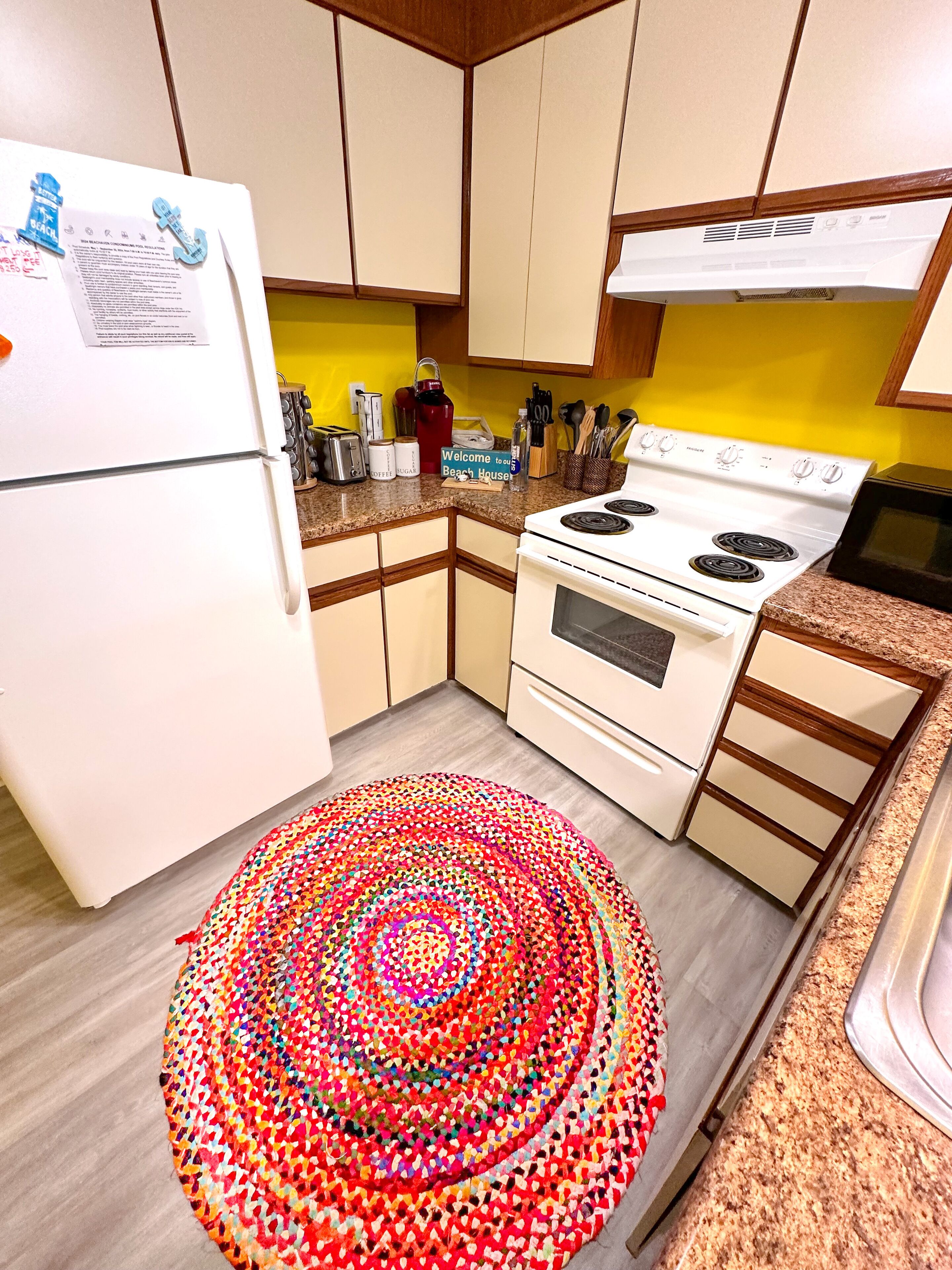 A kitchen with a white refrigerator, a stove, and a microwave. There is a colorful rug on the floor.