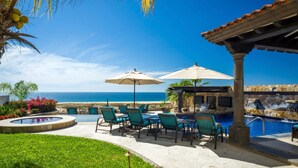 A pool area with lounge chairs and umbrellas, a view of the ocean, and a stone building with a water feature. - <br>CHRISTMAS & NEW YEARS EVE  4 BEDROOM LUXURY RESIDENCE AT QUIVIRA LOS CABOS (Cabo San lucas)