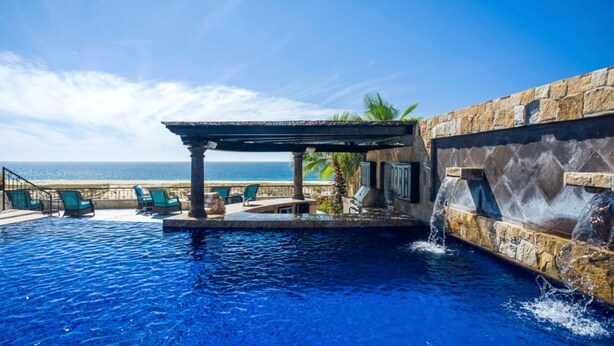 A pool area with a stone wall, a pergola, and a view of the ocean. - <br>CHRISTMAS & NEW YEARS EVE  4 BEDROOM LUXURY RESIDENCE AT QUIVIRA LOS CABOS (Cabo San lucas)