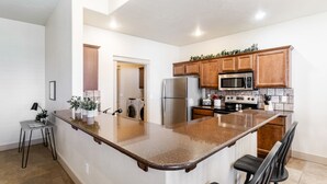 A modern kitchen with a large island, stainless steel appliances, wooden cabinets, and a small seating area. - TJ Rancher home, private yard, king beds, 2.5 bath (Twin Falls)