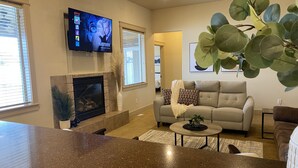 A living room with a fireplace, a sofa, a coffee table, and a television displaying 'GATSBY'. - TJ Rancher home, private yard, king beds, 2.5 bath (Twin Falls)