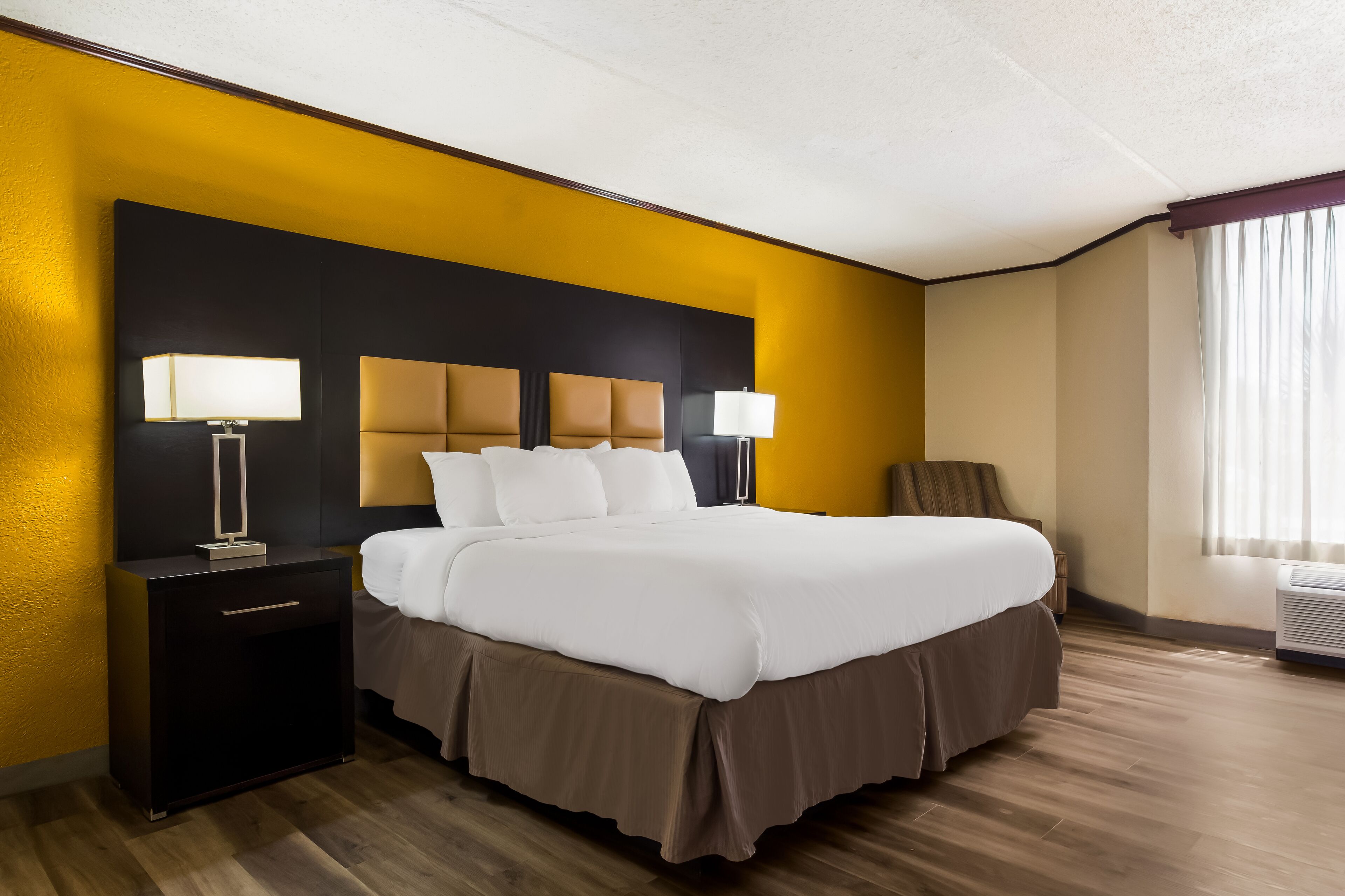 A hotel room with a large bed, bedside lamps, a nightstand, and a window with curtains.