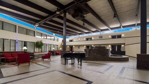 A spacious lobby with a piano, red sofas, and a fountain.