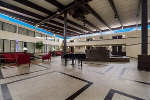 A spacious lobby with a piano, red sofas, and a fountain.