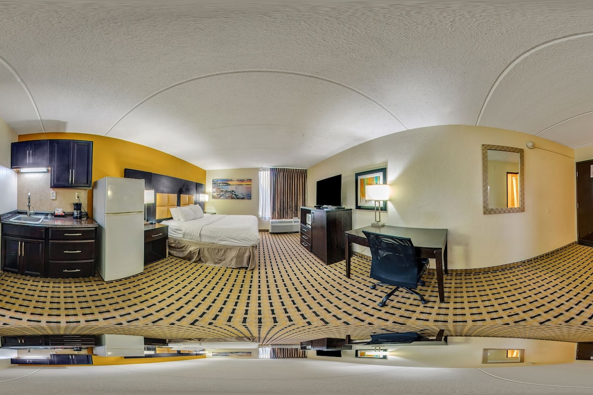 A panoramic view of a hotel room with a kitchen area, a bed, and a desk.