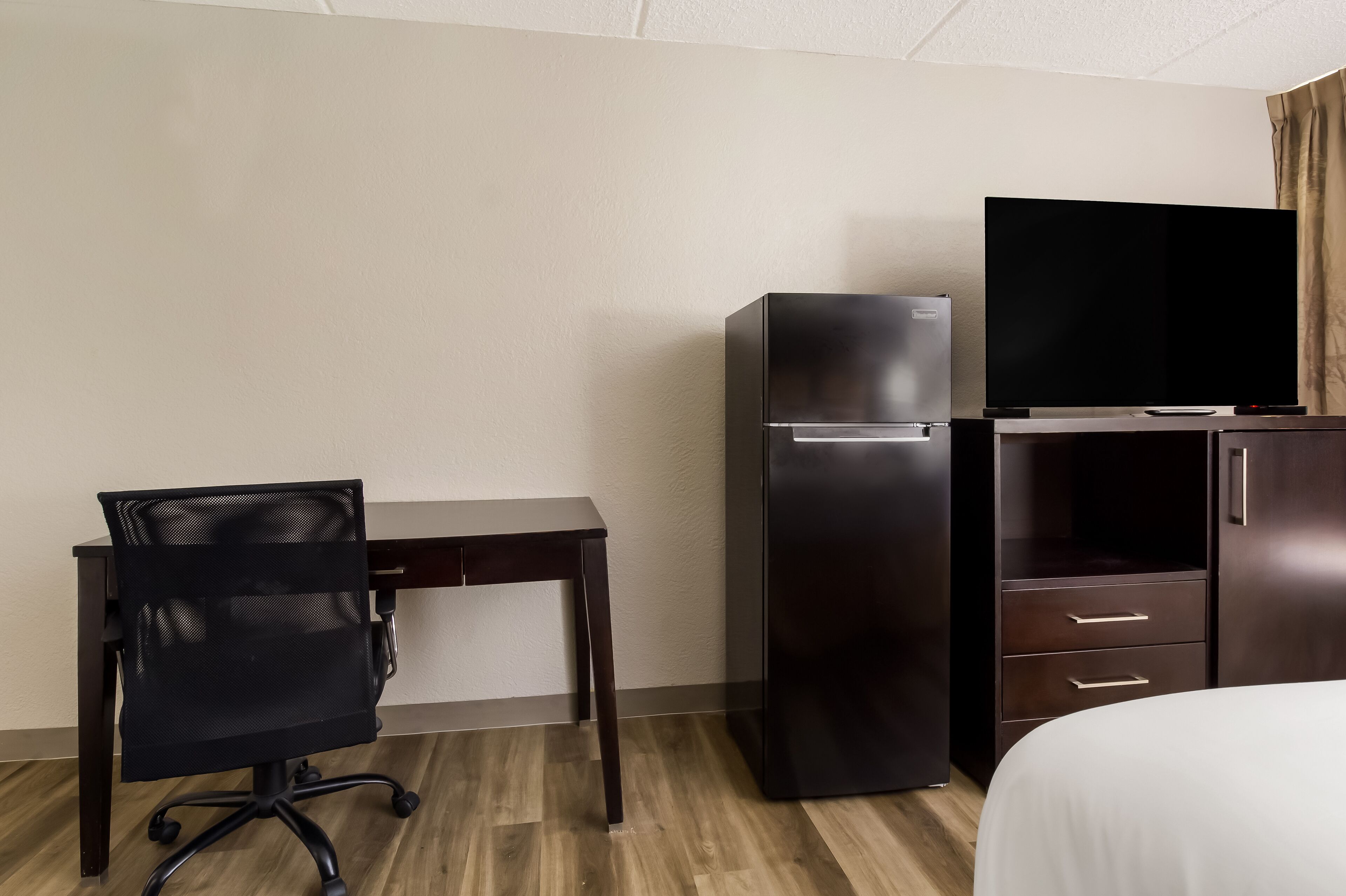 Habitación de hotel con una cama, un escritorio con silla, un refrigerador y un televisor.