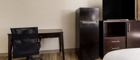 Habitación de hotel con una cama, un escritorio con silla, un refrigerador y un televisor.