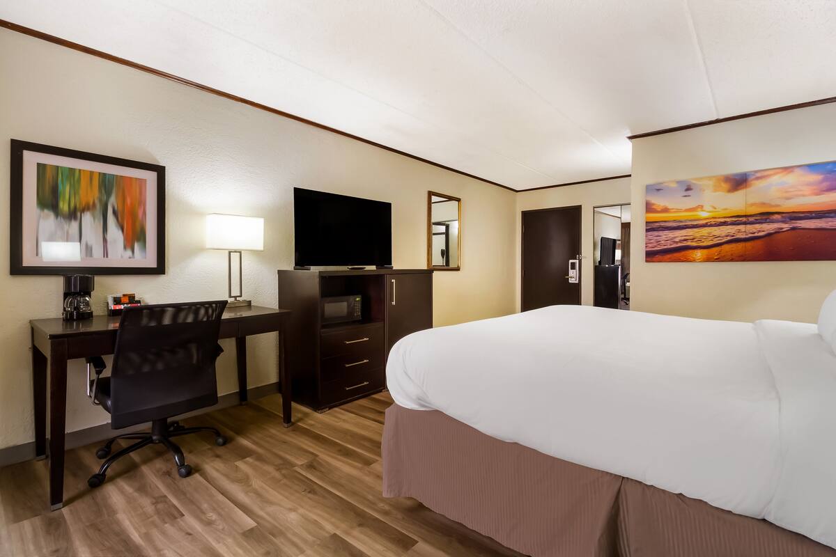 A hotel room with a bed, desk, chair, TV, and artwork on the walls.