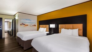 A hotel room with two beds, a wooden floor, a yellow accent wall, and a painting of a beach scene.