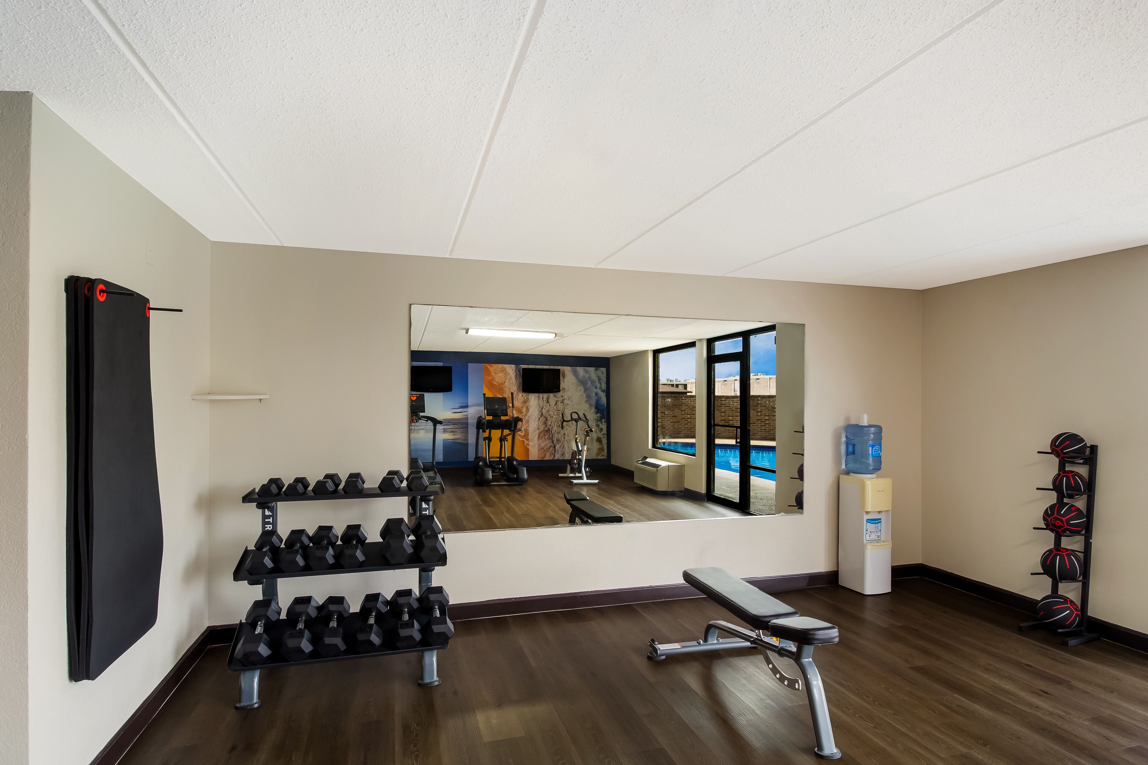A gym with a mirrored wall, dumbbells, a bench, and a water dispenser.