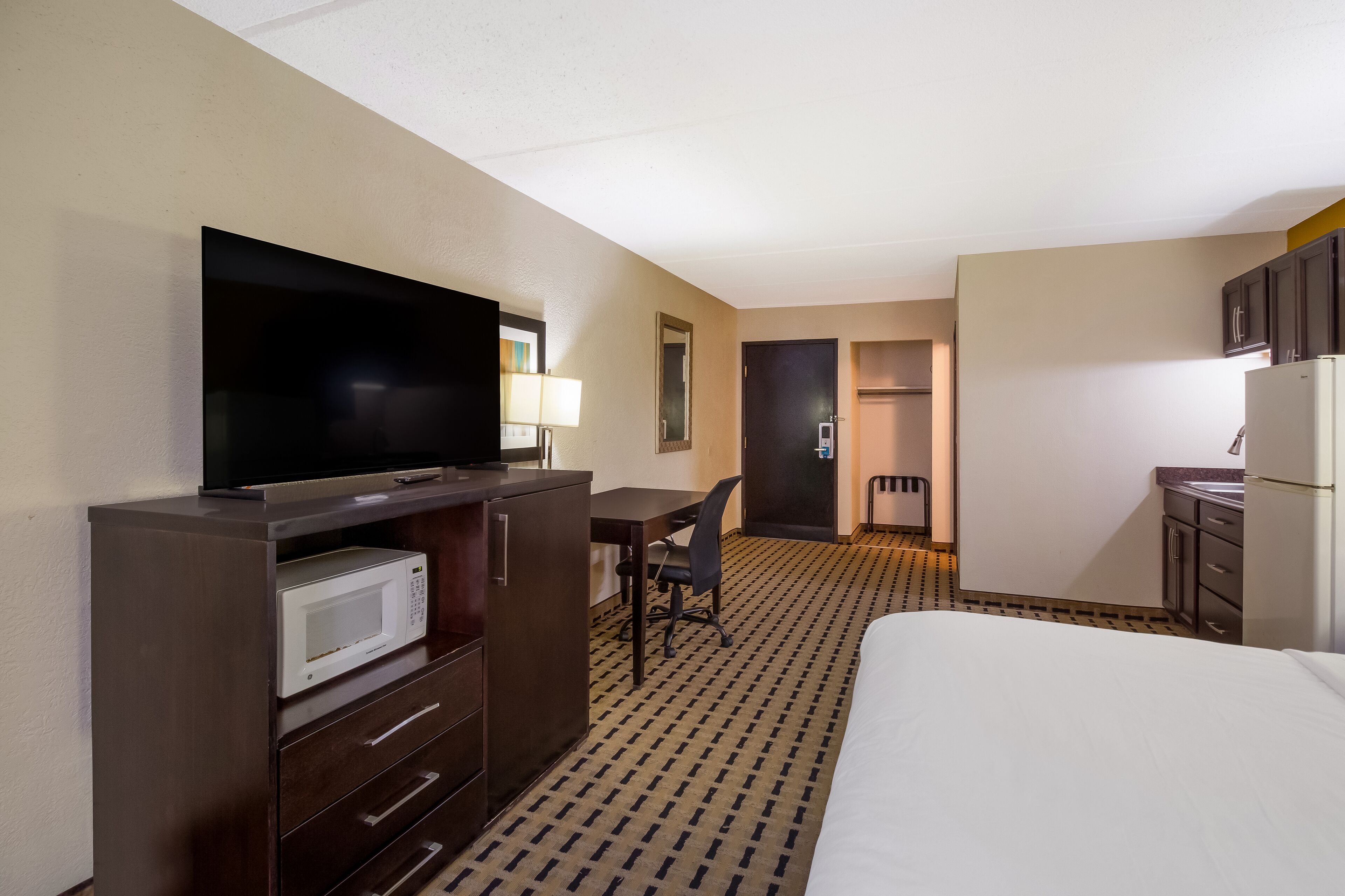 A hotel room with a bed, a desk with a chair, a television, a microwave, a refrigerator, and a bathroom.