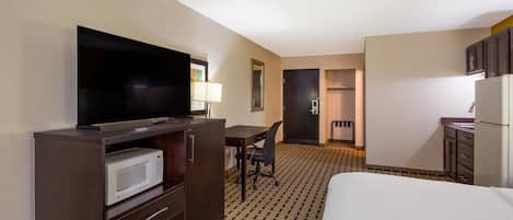 Habitación de hotel con cama, escritorio y silla, televisor, microondas, refrigerador y baño.