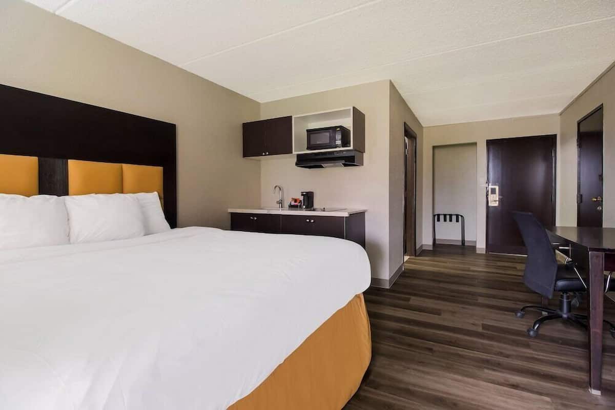 A hotel room with a large bed, a desk, a microwave, and a door leading to another room.