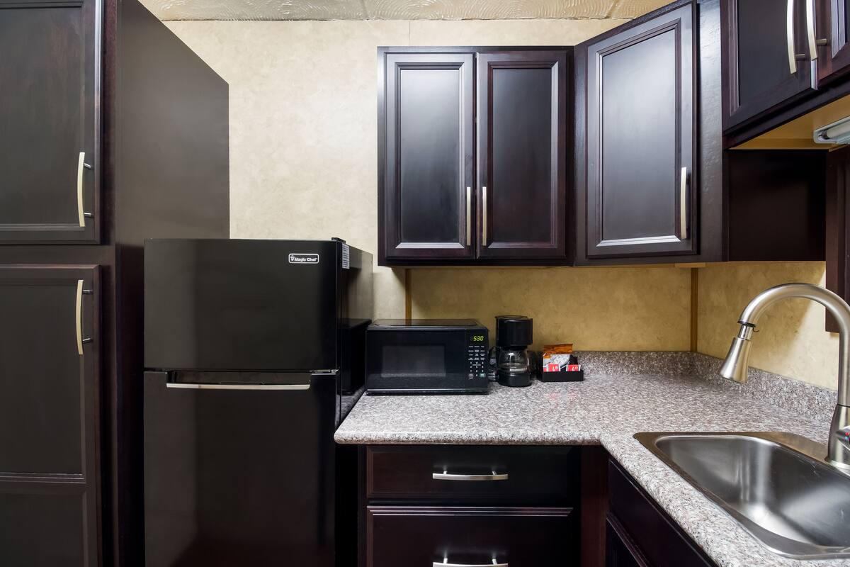 A compact kitchen with dark cabinets, a black refrigerator, a microwave, a coffee maker, and a sink.
