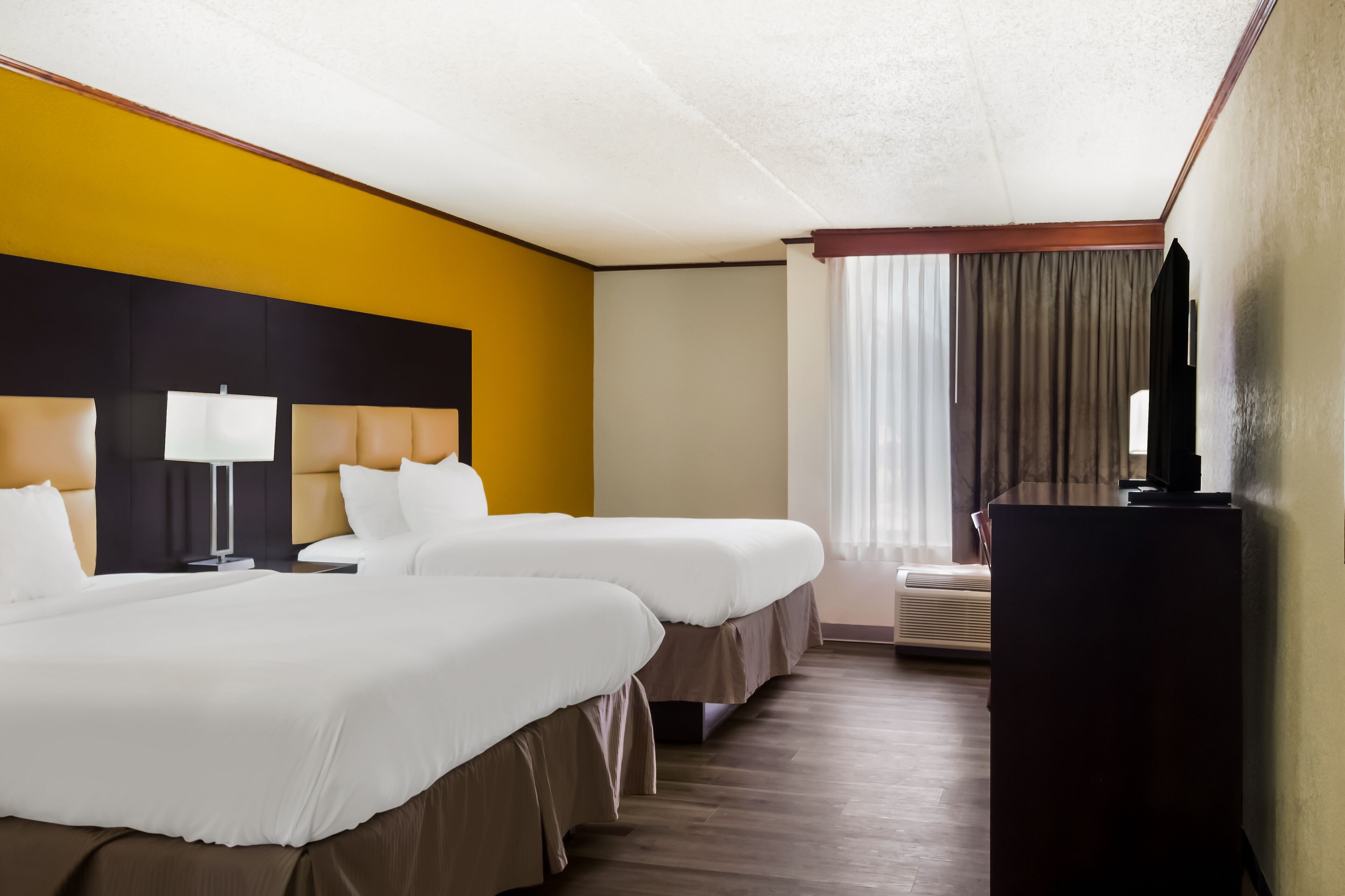 Quarto de hotel com duas camas, uma escrivaninha, uma televisão e uma janela com cortinas.