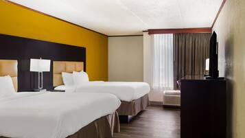 Quarto de hotel com duas camas, uma escrivaninha, uma televisão e uma janela com cortinas.