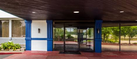 A building entrance with a dark wooden ceiling, glass doors, and a red brick pathway.