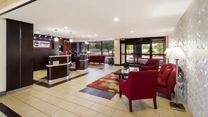 A hotel lobby with a reception desk, red seating, a patterned rug, and a wall with hexagonal patterns.