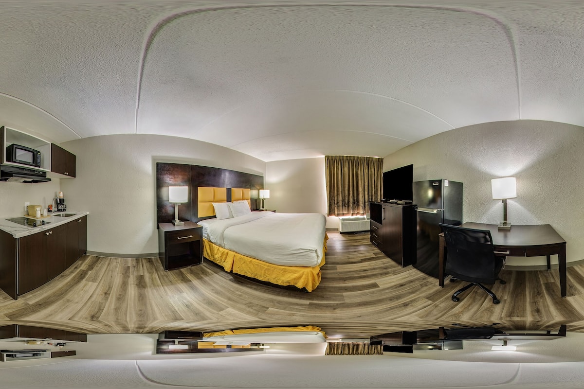 A panoramic view of a hotel room with a bed, desk, and seating area, featuring a modern design and wooden flooring.