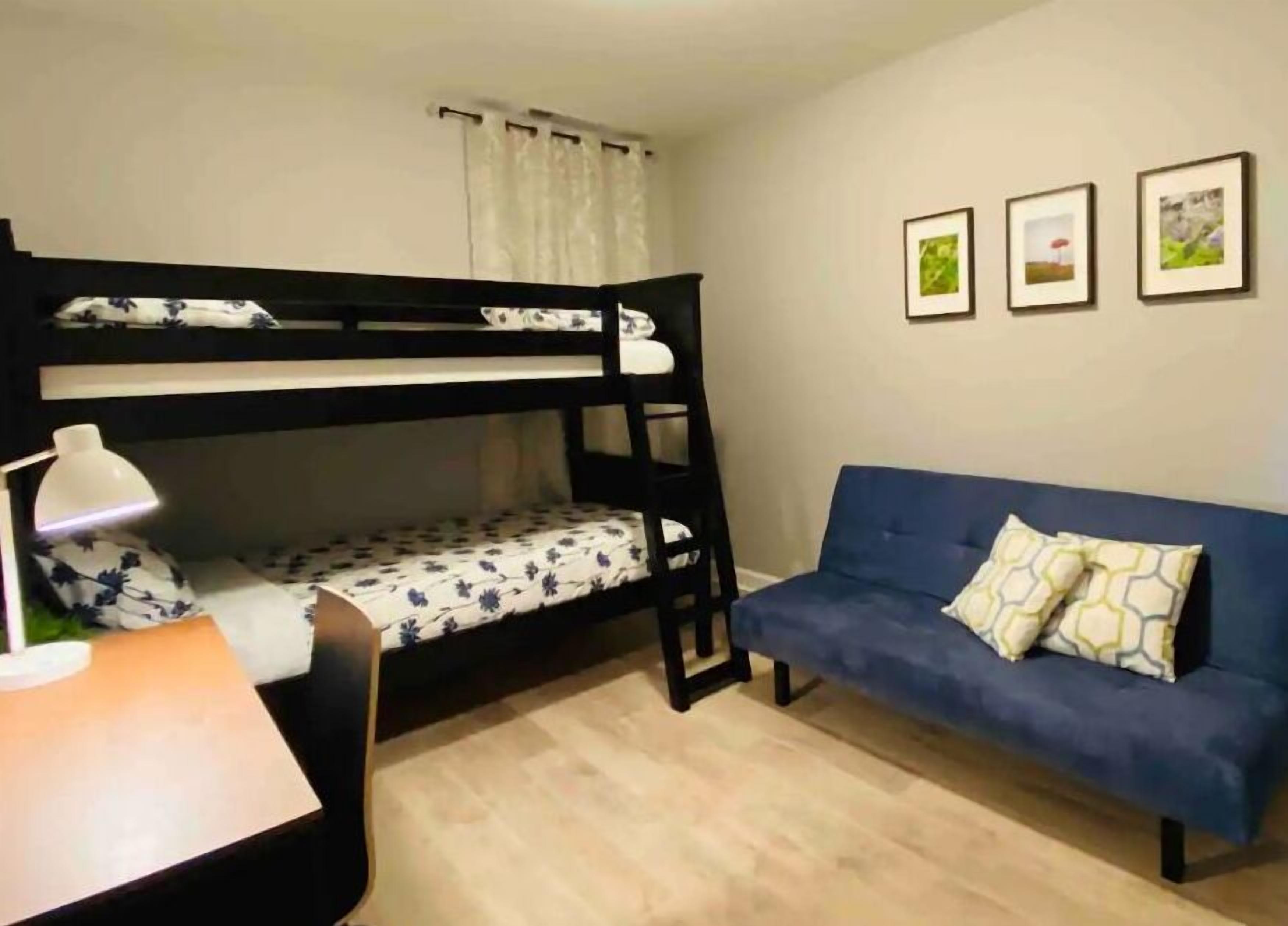 A room with a bunk bed, a desk with a lamp, a blue sofa, and three framed pictures on the wall.