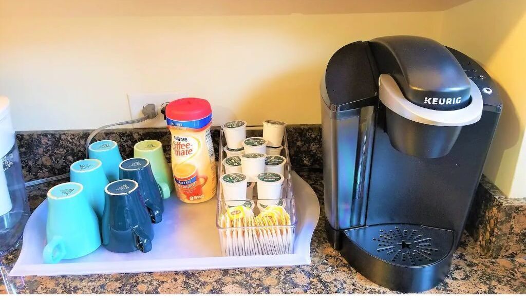 Una cafetera, un soporte para cápsulas de café y varias tazas de café sobre una encimera de cocina.