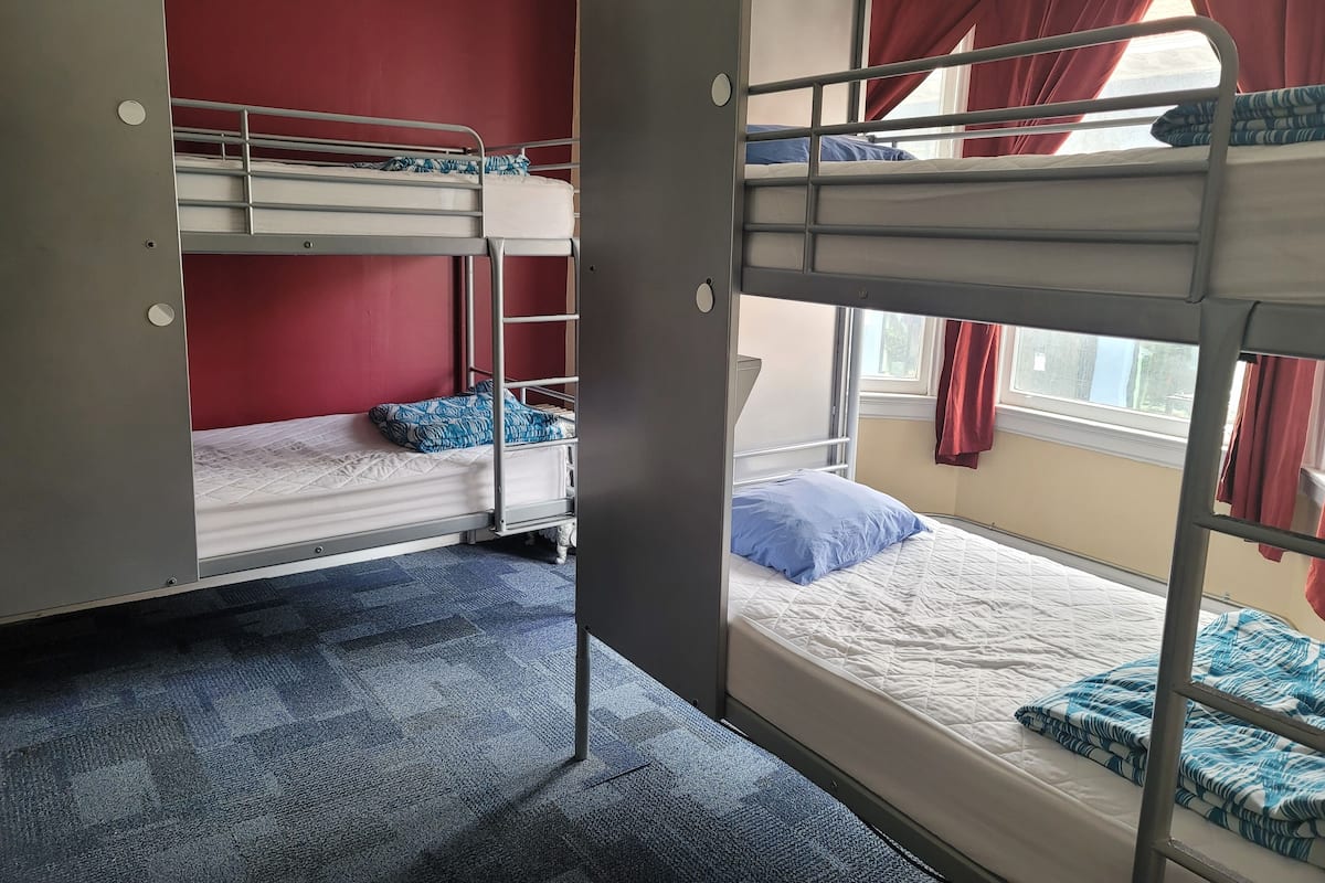 A dormitory room with bunk beds, red walls, and a window with curtains.