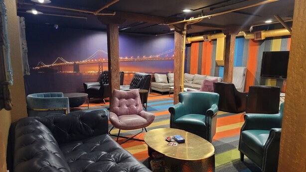A lounge area with leather sofas, armchairs, and a coffee table. A mural of a bridge is visible in the background. - Ansonia Hotel - Hostel (San Francisco)