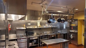 A commercial kitchen with stainless steel appliances, a microwave, and hanging pots. - Ansonia Hotel - Hostel (San Francisco)