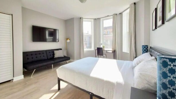 Et moderne hotelværelse med en stor seng, en sofa, et skrivebord og et fjernsyn ophængt på væggen.