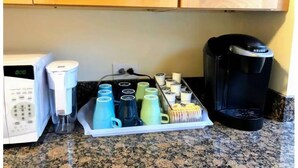 Et køkken med kaffemaskine, kaffemaskine og bakke med kaffekopper.