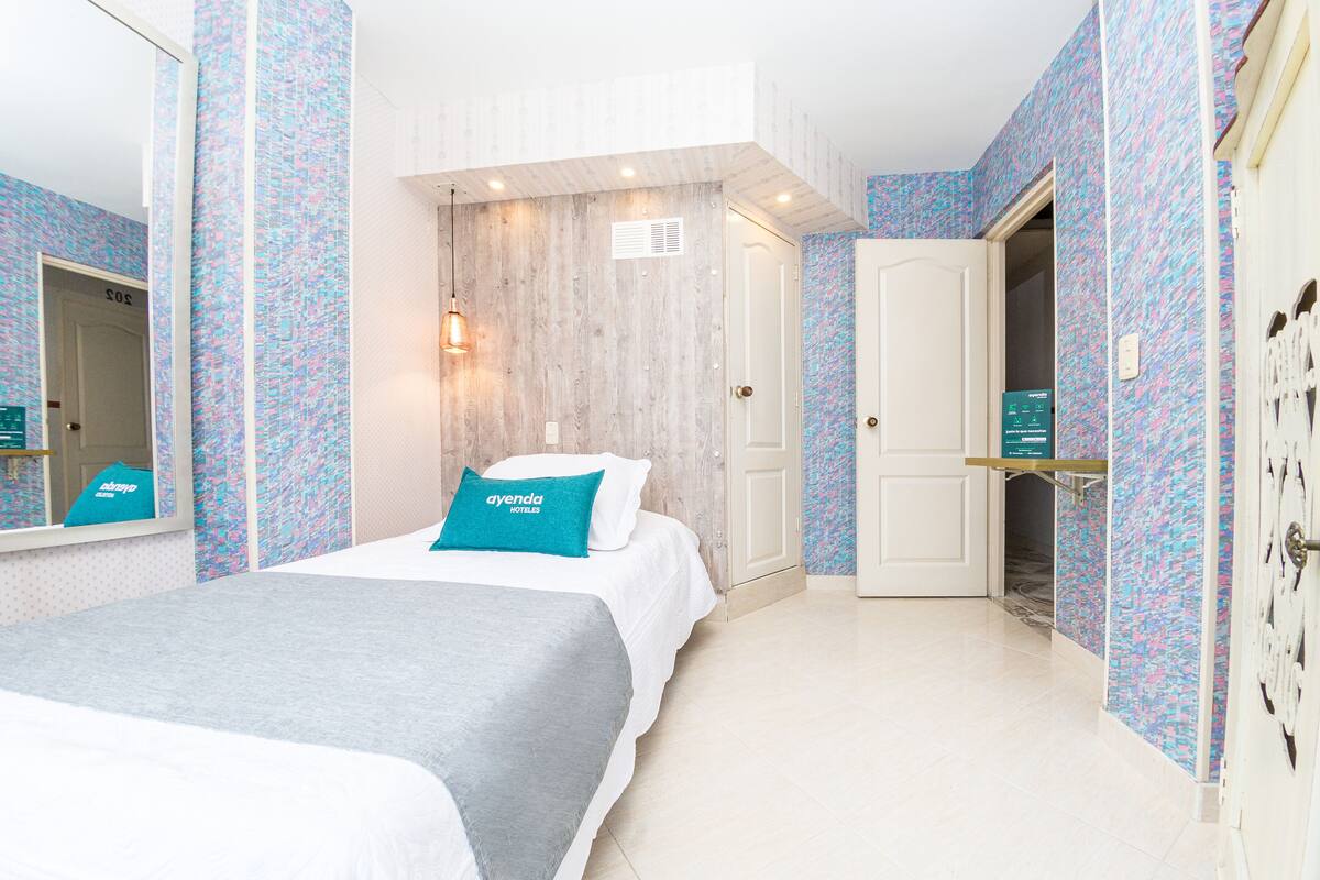 Una habitación de hotel con cama, armario, espejo y una puerta que da a otra habitación.