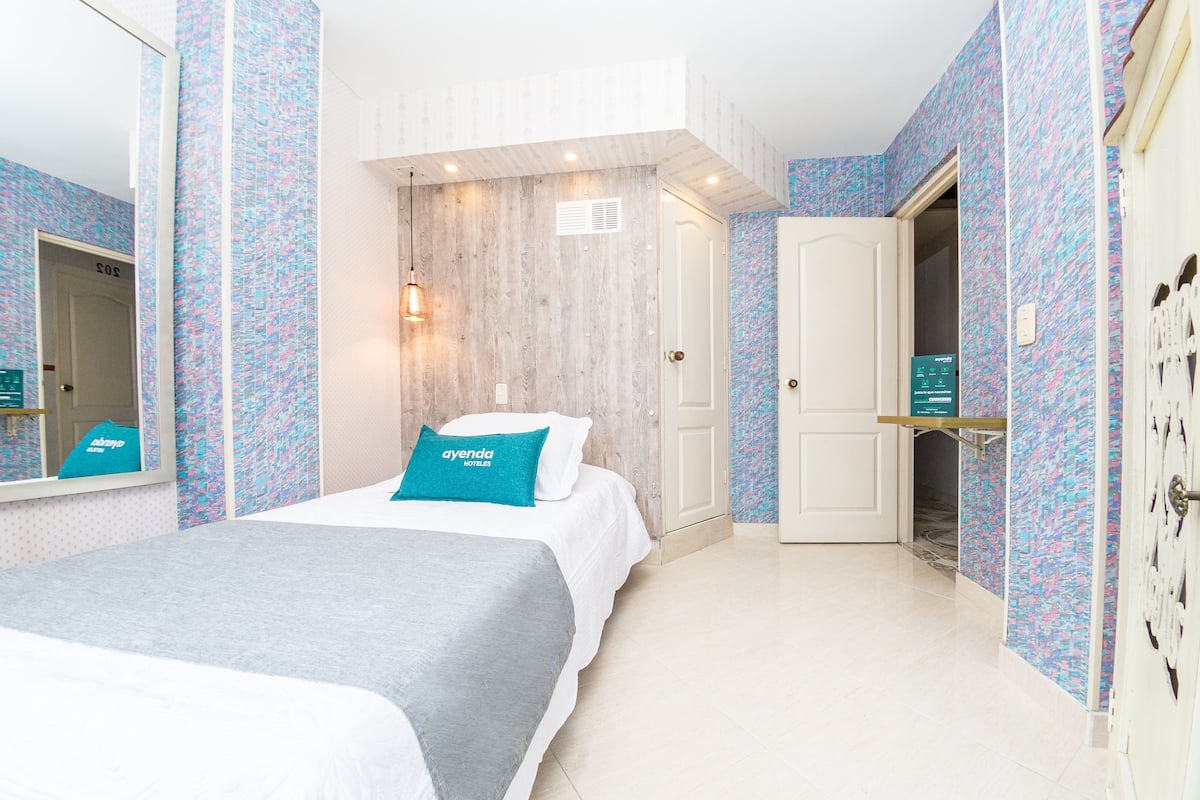 Habitación de hotel con cama, armario, espejo y puerta que da al baño.