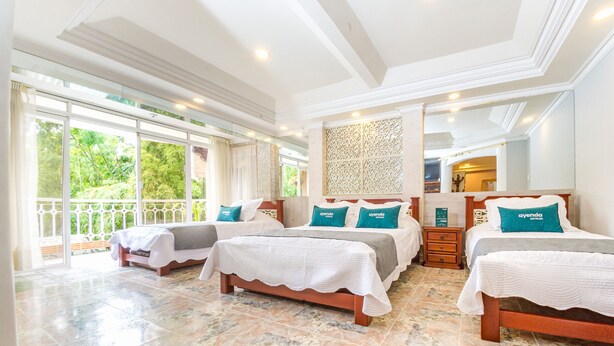 Habitación de hotel con tres camas, un ventanal grande y un balcón.