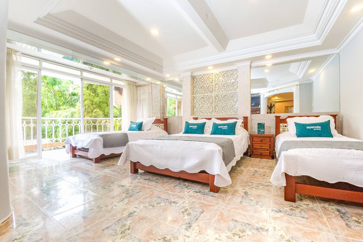 Habitación de hotel con tres camas, un ventanal grande y un balcón.