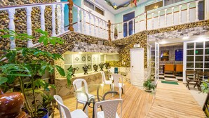 Un espacio interior amplio con piso de madera, sillas blancas, una mesa de vidrio y una pared de piedra.