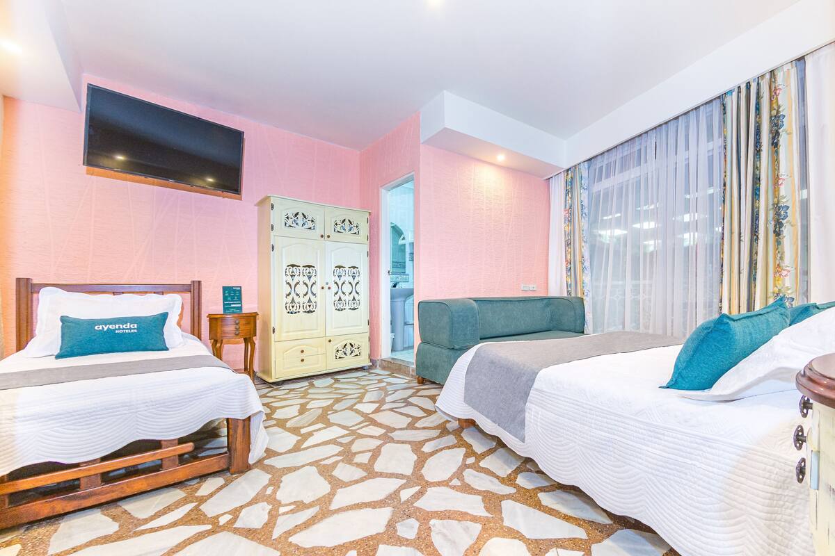 Habitación de hotel con dos camas, un armario, televisión y suelo estampado.