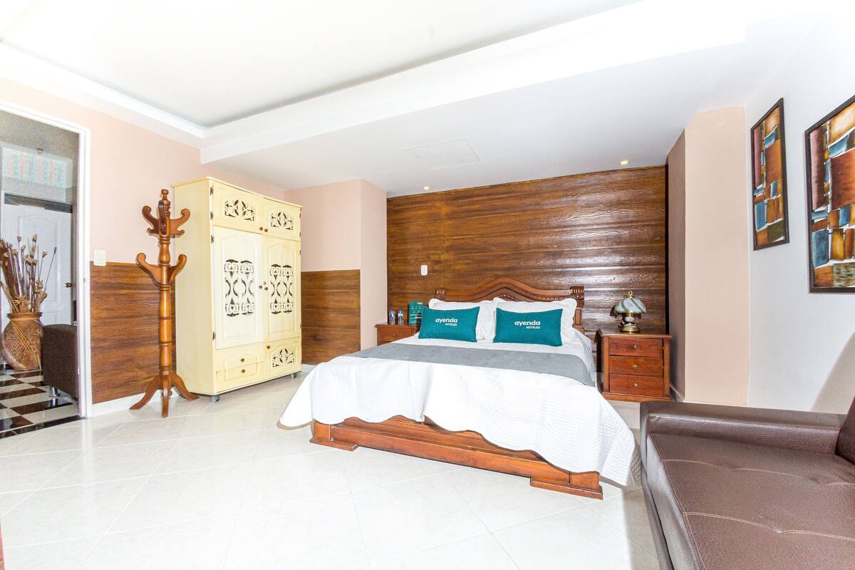 Un dormitorio con una cama de madera, un armario, una mesita de noche y un sofá de cuero marrón.