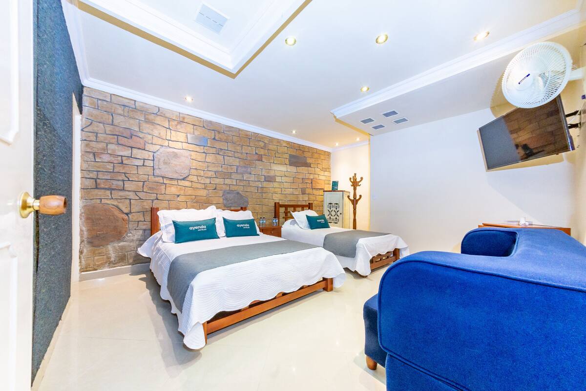 Habitación de hotel con dos camas, una pared de piedra, un televisor montado y un ventilador de techo.