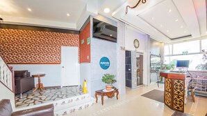 Un vestíbulo de hotel con mostrador de recepción, zona de estar y una escalera que conduce a otro piso.