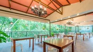 Un comedor interior con mesas de madera y sillas blancas, ventanas amplias con vistas a zonas verdes y un candelabro.