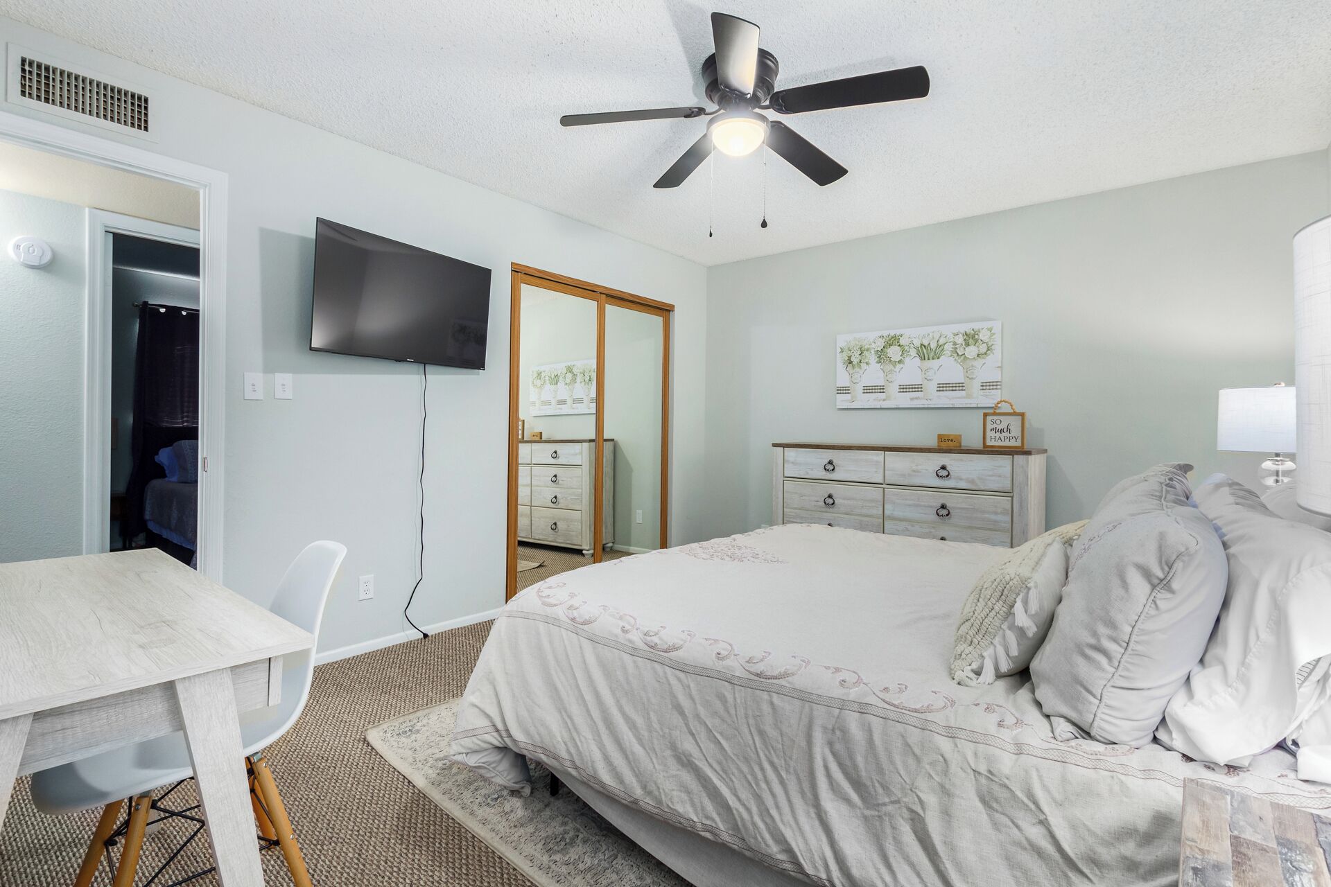 Une chambre à coucher comprenant un lit, un bureau, une chaise, un ventilateur de plafond, une télévision et une commode.