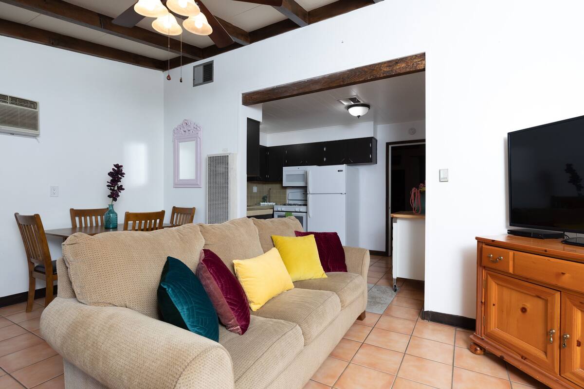 A living room with a beige sofa, colorful cushions, a wooden cabinet, and a television.