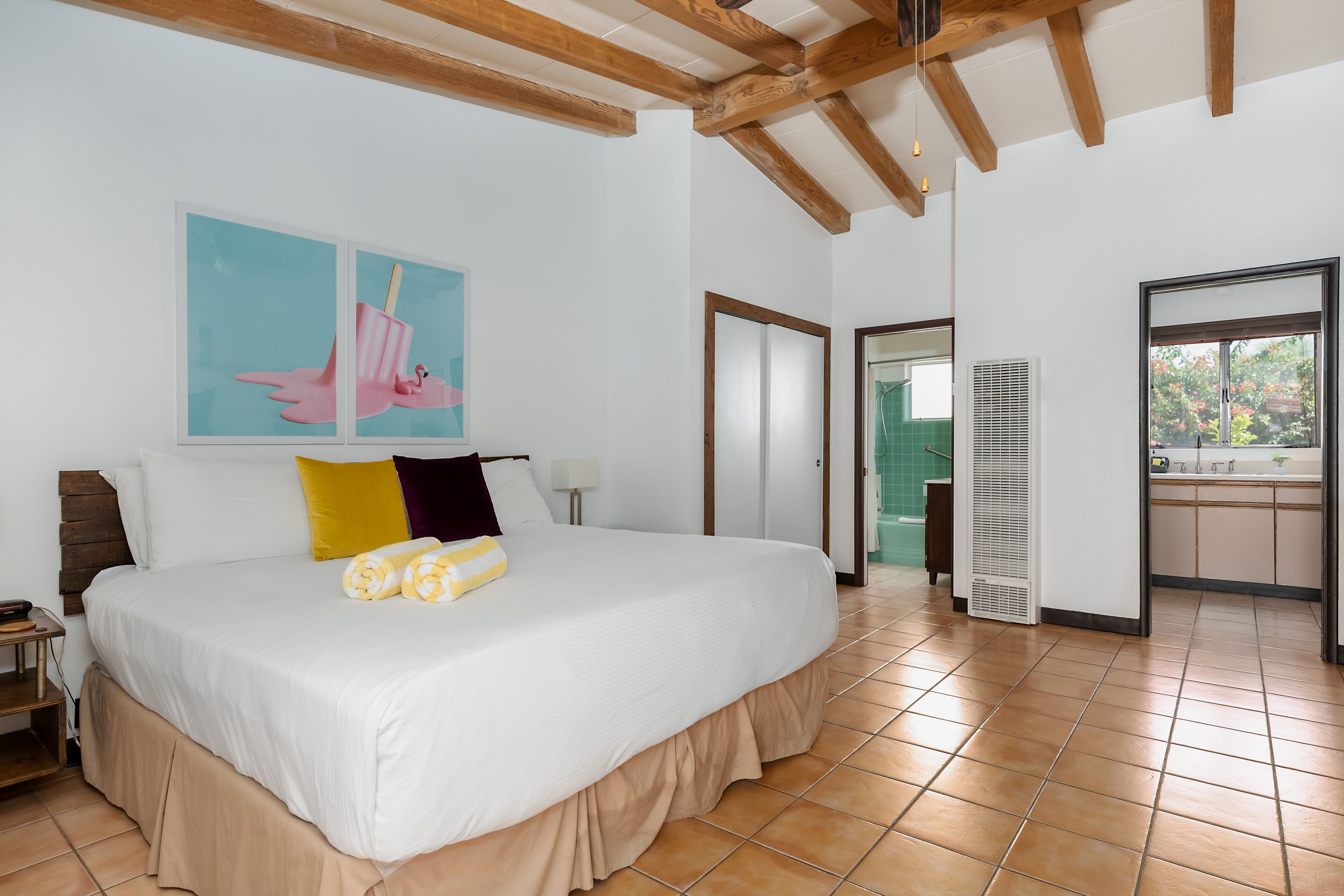 Un dormitorio amplio con una cama grande, vigas de madera, un baño con ventana y una zona de cocina.