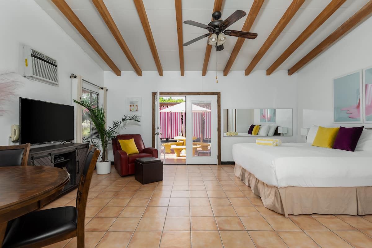 A hotel room with a bed, a TV, a dining table, and a ceiling fan.