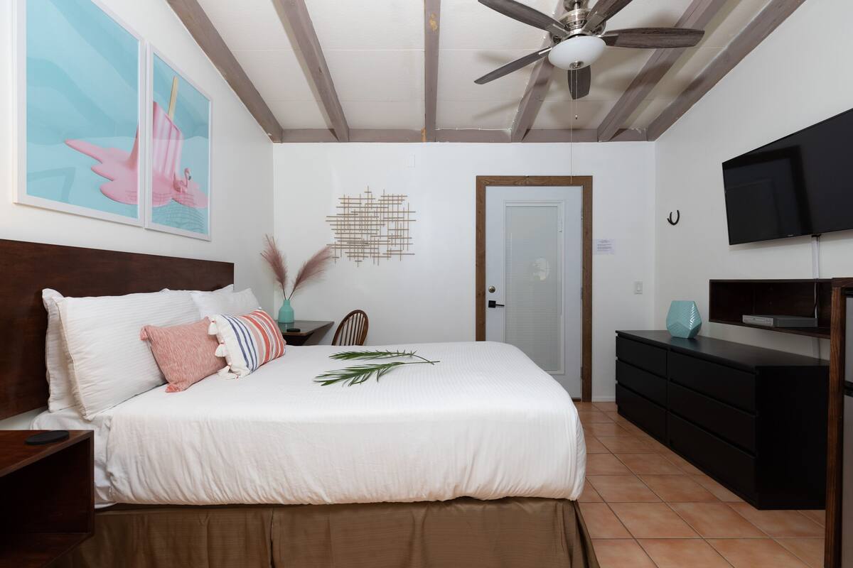 A bedroom with a bed, a nightstand, a dresser, a television, and a ceiling fan.