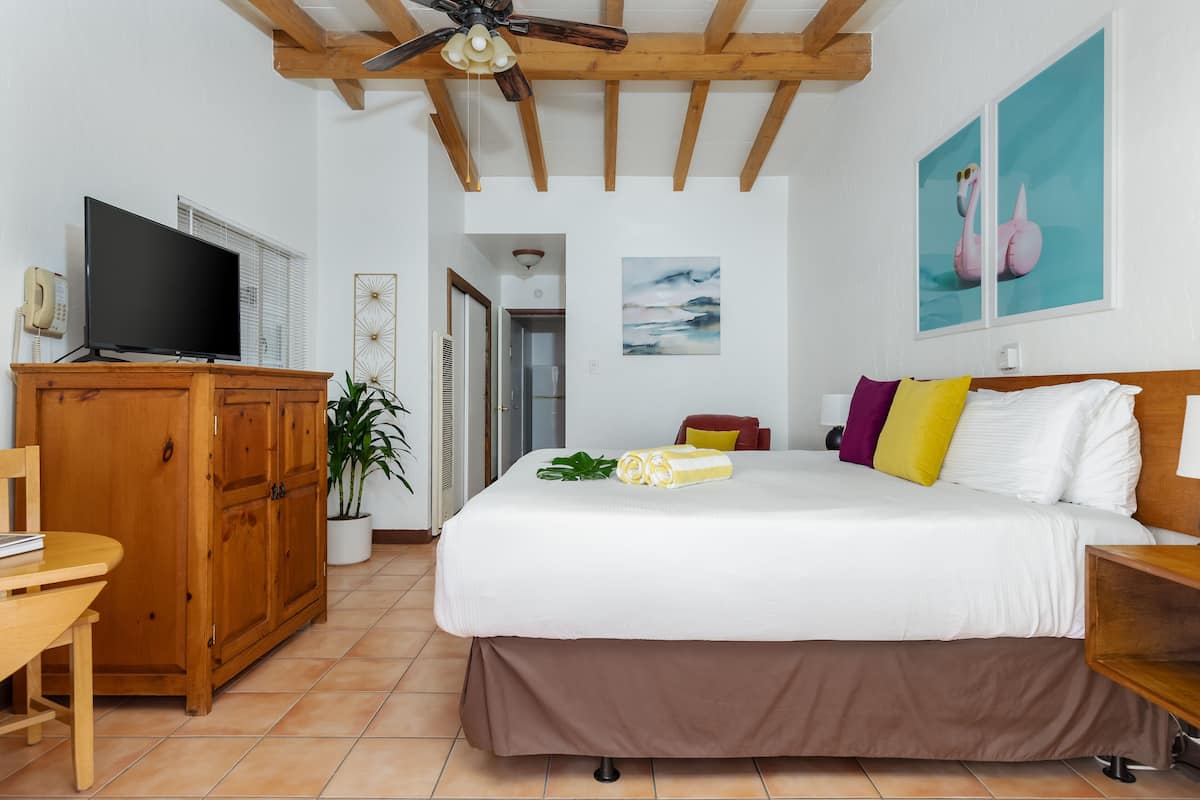 A hotel room with a bed, wooden furniture, a television, and a ceiling fan.