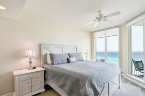 Een slaapkamer met een groot bed, een nachtkastje, een plafondventilator en uitzicht op de oceaan.