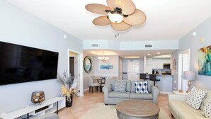 A living room with a flat-screen TV, a ceiling fan, a round coffee table, and a sofa.