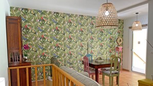 Une pièce avec un escalier en bois, un papier peint à motifs, une table à manger avec des chaises et des lampes suspendues.