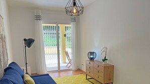 Une pièce avec un canapé bleu, une commode en bois, une lampe et une vue sur un espace extérieur, visible à travers une porte vitrée.